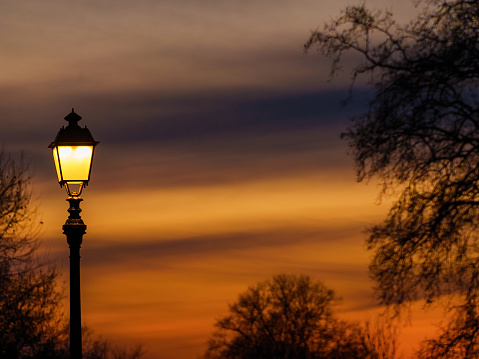 Old fashioned street lamp against beautiful sunset sky and bare tree branches silhouettes