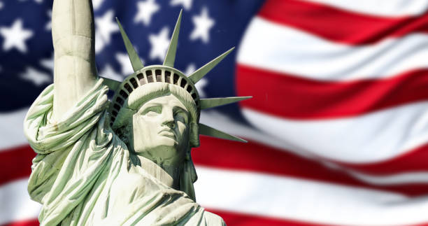 the statue of liberty with blurred american flag waving in the background - estátua da liberdade imagens e fotografias de stock