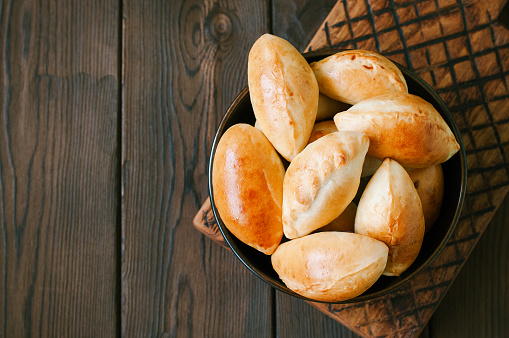 Potato stuffed hand pies - pirozhki in a black bowl on a wooden board. Top view and copy space.