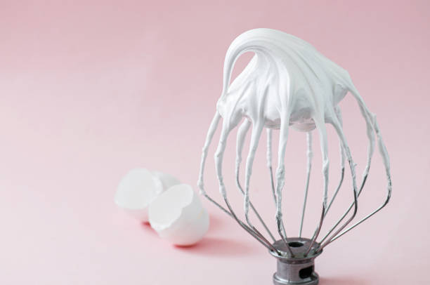 claras de huevo batidas: merengue italiano batido en un batidor de alambre y cáscaras de huevo sobre fondo rosado. - batidora eléctrica fotografías e imágenes de stock