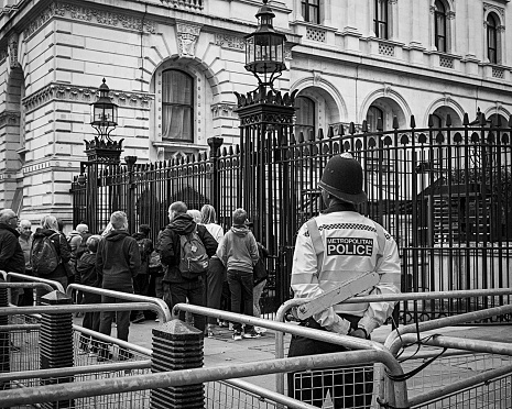 A gathering of adults and children outside the gates to Downing Street in Whitehall, London, with a Metropolitan Policeman watching.