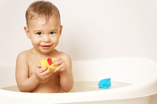 Adorable little boy is playing with a rubber duck while taking a bath in warm water.