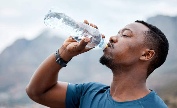 colpo di un giovane sportivo che beve acqua mentre si allena all'aperto - drinking men water bottle foto e immagini stock