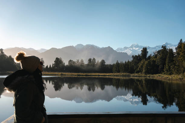 женщина смотрит на горы, отражающие озеро мэтисон, новая зеландия - glacier west coast south island new zealand people стоковые фото и изображения