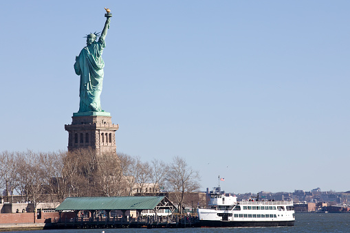 Statue of Liberty International Landmark at Liberty Island. Tour boat with tourists docked at site.