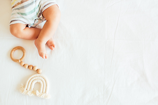 Baby playing with a wooden toy on white linens background. Mockup. Top view. Copy space.