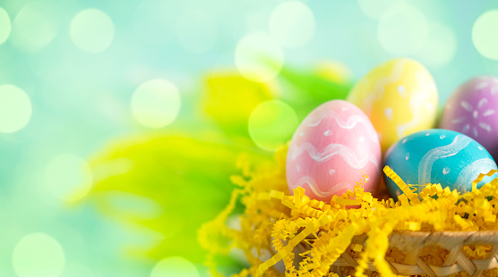 Multi colored hand-painted Easter eggs in a basket. Defocused lights (bokeh) background. Space for copy.