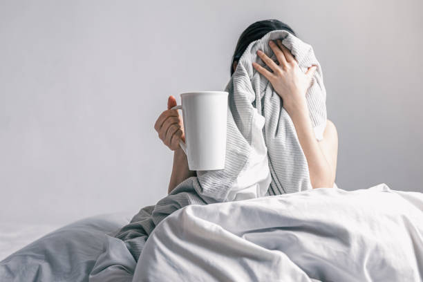 istock A woman holds a cup of coffee while lying in bed. 1370570860