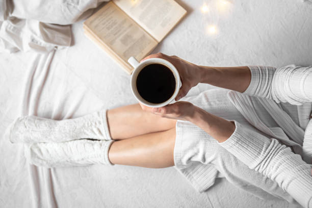 istock Cup of coffee in female hands in bed, top view. 1370570871