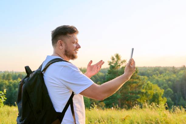 istock Middle aged bearded man with smartphone backpack on hike, making video call 1370572591