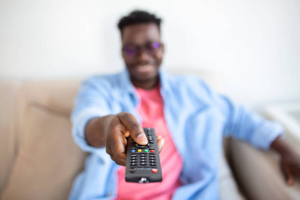 istock Excited African American Man Pointing Television Controller To Camera Switching Channels Watching TV . Television Programming Advertisement. Selective Focus 1370573259