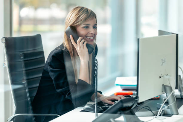 istock Beautiful young business woman working with computer while talking to office phone in modern startup office. 1370574409