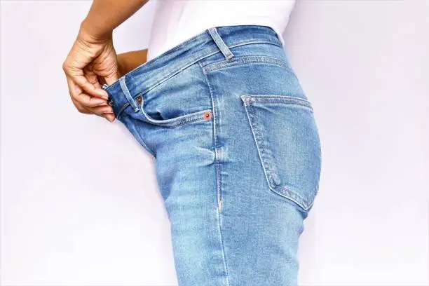 Weight loss concept, body part of woman wearing loose pants blue jean photo isolate on white background side view copy space