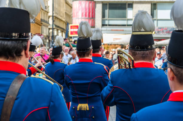 A lively Bavarian parade scene featuring drummers in traditional Lederhosen and Dirndls marching along a sunny street, crowds watching, and a festive atmosphere of culture and music.