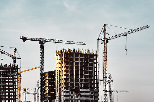 Construction site with frames of multistory buildings and cranes at clear blue sky background