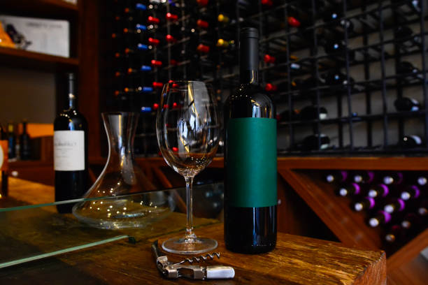 istock Red wine bottle with green label, wine glass and corkscrew on rustic wooden table in a charming restaurant cellar. Wine bottle mockup 1370584084