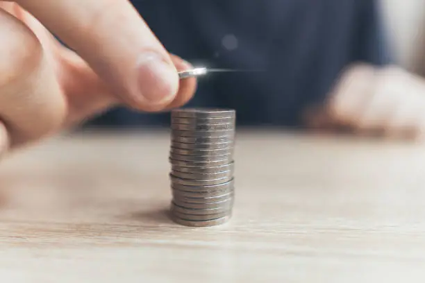 Photo of The person puts the coins into a stack of money. The concept of capitalization and investment