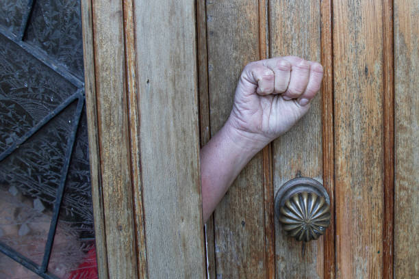 istock domestic violence, asking for help, a woman's hand makes a sign asking for help from a closed door, palm to camera and tuck thumb 1370585285