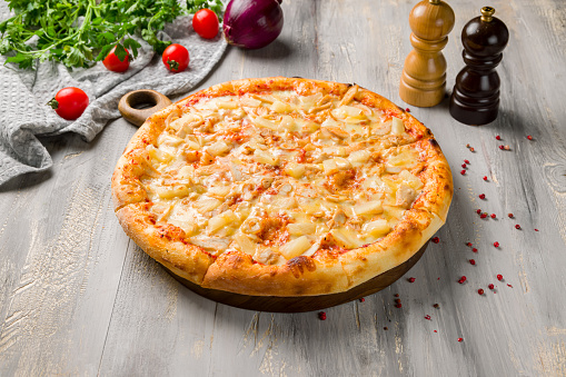 pizza Hawaiian with pineapple and chicken on grey wooden table