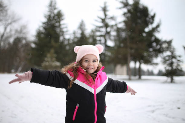 Joyful kid in winterwear looking at camera in natural environment in winter