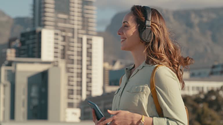 4k video footage of a young woman wearing headphones and using her cellphone while out in the city