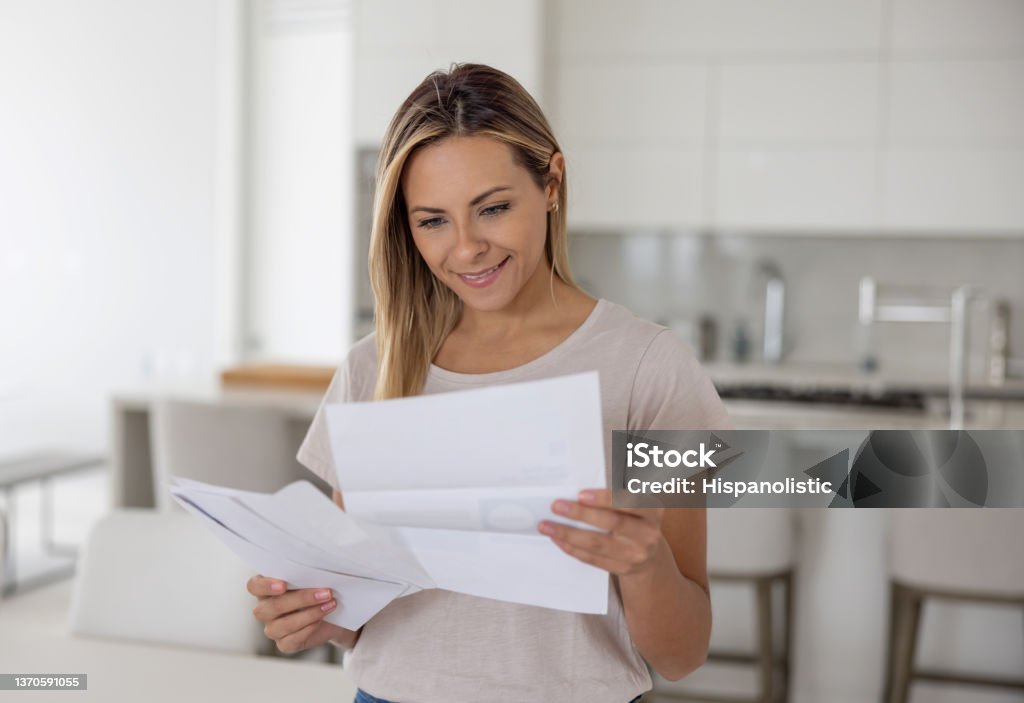 Woman at home reading a letter in her mail Happy Latin American woman at home checking a letter in her mail and smiling - domestic life concepts Letter - Document Stock Photo