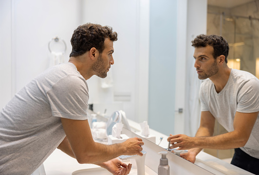 Handsome Latin American man washing his hands in the bathroom while looking in the mirror - domestic life concepts