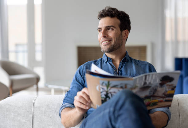 homme à la maison lisant un magazine dans le salon - reading newspaper men magazine photos et images de collection