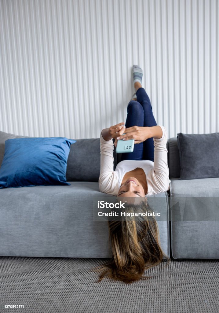 Happy woman at home texting on her cell phone Happy woman at home texting on her cell phone while sitting upside-down on the sofa Upside Down Stock Photo