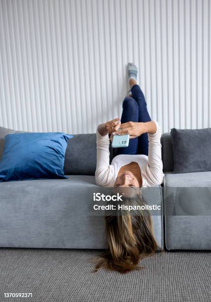 Happy Woman At Home Texting On Her Cell Phone Stock Photo - Download Image Now - Upside Down, Sofa, Women