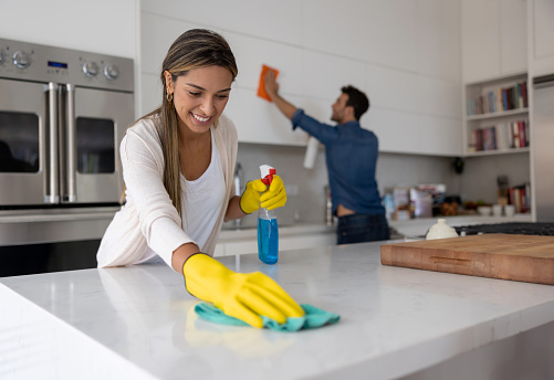 Happy Latin American couple at home cleaning the kitchen - domestic life concepts