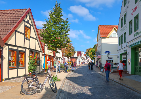 The narrow cobbled street of shops, small homes and cafes in the historic section of Warnemunde Germany, filled with tourists at summer.