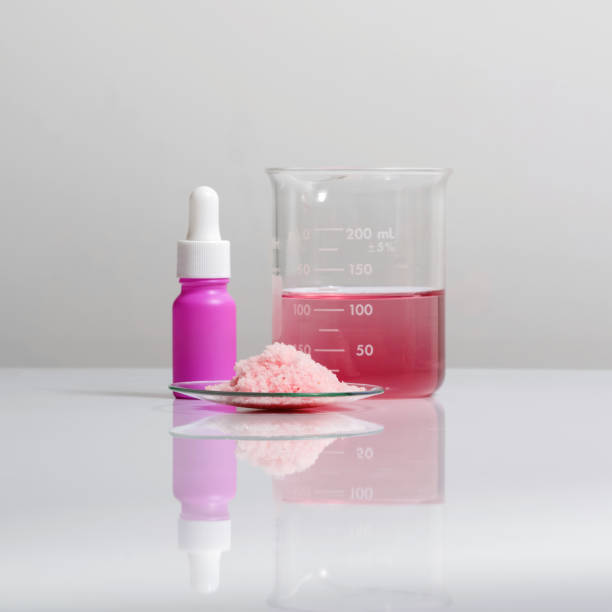 Chemicals for beauty care on white laboratory table. Pink flake chemicals in Chemical Watch Glass place next to Serum bottle with dropper and Red EPOXY liquid rasin in beaker. productos químicos para el cuidado de la belleza en una mesa de laboratorio blanca. productos químicos en escamas rosadas en chemical watch glass colocar junto a la botella de suero con gotero y rasina líquida epoxy roja en el vaso de precipitados.