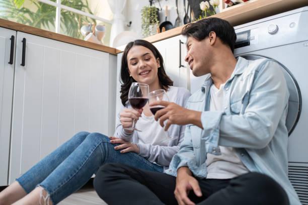 jovem casal asiático novo casamento passar um tempo juntos na cozinha em casa. homem e mulher românticos atraentes se sentam no chão aproveitem o vinho para celebrar a vida familiar e se mudarem para uma nova casa. - japanese ethnicity heterosexual couple men smiling - fotografias e filmes do acervo