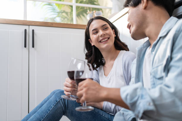 um jovem casal asiático passa um tempo juntos na cozinha de casa. homem e mulher românticos atraentes se sentam no chão para beber vinho para celebrar a vida familiar e se mudar para uma nova casa. - japanese ethnicity heterosexual couple men smiling - fotografias e filmes do acervo