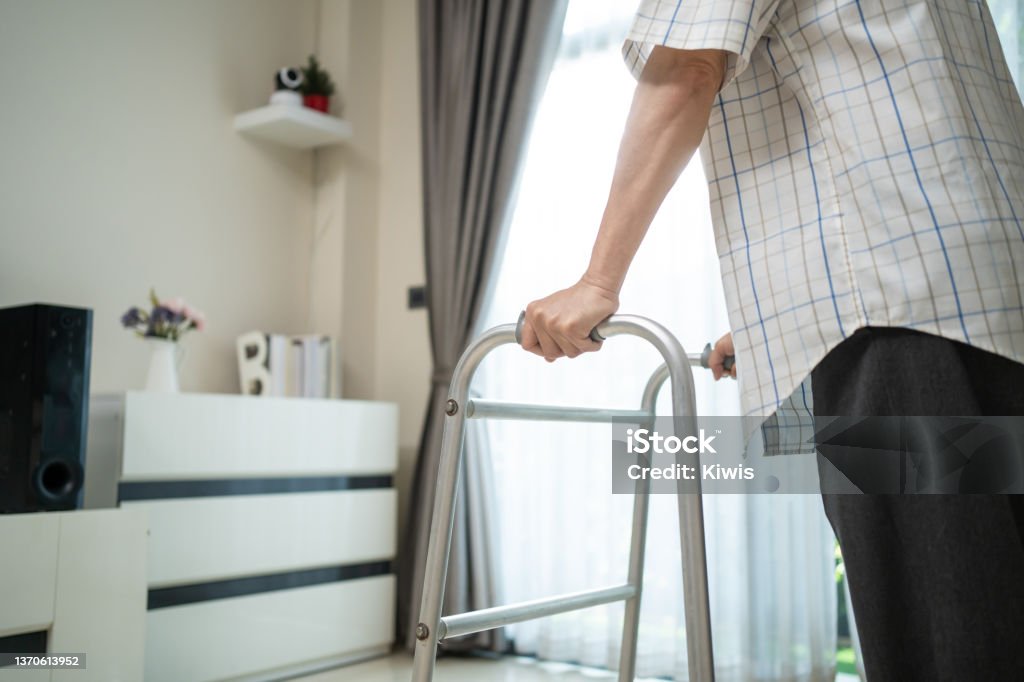 Close up hand of Senior disabled man walk with walker at nursing home. Asian Older elderly handicapped male patient have weak leg slowly use Zimmer frame to support. Medical therapy insurance concept. Civilian Stock Photo