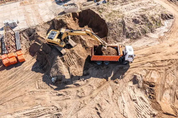 loader excavator loads the ground in the truck on construction site. aerial overhead view.