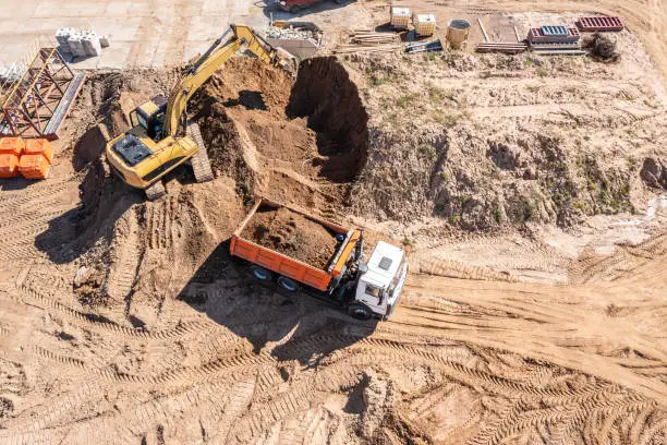 excavator loads sand into a truck on construction site. aerial top view from a drone.