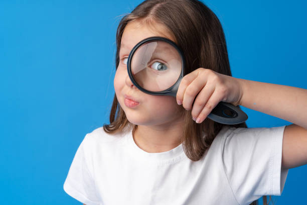 istock Little girl looking through a magnifying glass on blue background 1370628527