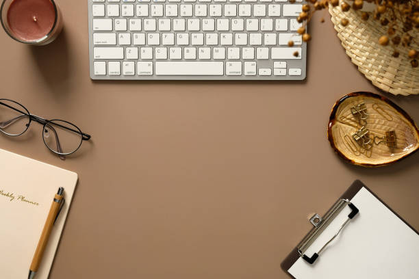 istock Elegant feminine workspace. Keyboard, weekly planner, notepad, office stationery, candle, dried flowers on brown background. Flat lay, top view. 1370631723