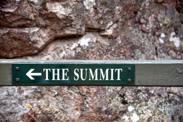 A green sign is indicating the direction to the summit in front of a natural rock face background