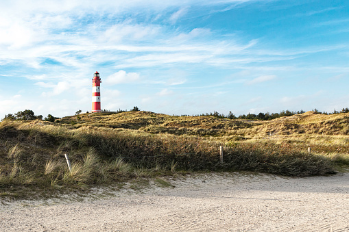 Summer evening view on maritime lighthouse and sandy grassy landscape around. Sandy dirt road for bikers and walkers in foreground.