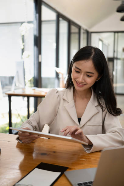 istock Cheerful asian woman using digital tablet while sitting in modern office. 1370642613