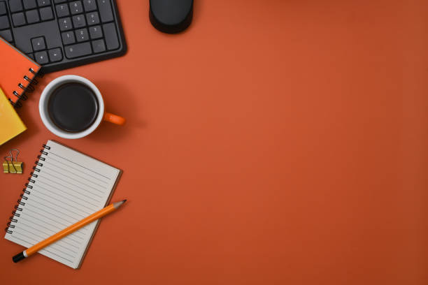 istock Top view coffee cup, notebook and keyboard on orange background. 1370643048