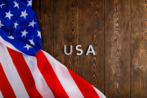 the word USA laid with silver metal letters on wooden board surface with crumpled flag of United States of America in directly above perspective