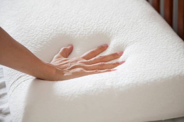 woman holding white thin memory foam pillow on white bedsheets stock photo