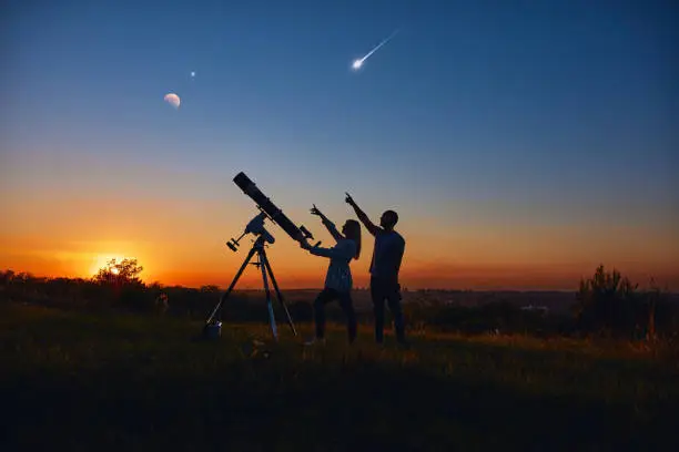 Photo of Couple stargazing together with a astronomical telescope.