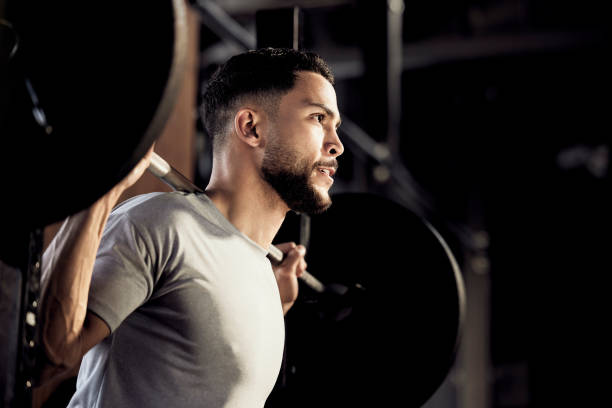 foto de un joven musculoso haciendo ejercicio con un peso en un gimnasio - levantamiento de pesas fotografías e imágenes de stock