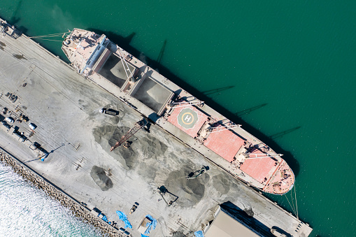 Aerial view of a large cargo ship being loaded with cement in an international port. Sea transportation.