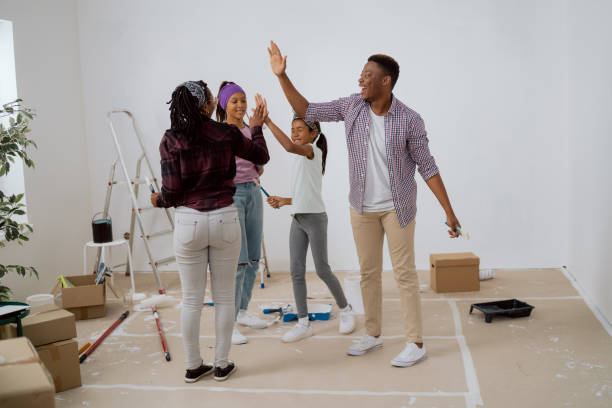 el equipo de la familia trabaja en conjunto durante la renovación del apartamento, los niños de cinco años con sus padres después de pintar con éxito las paredes alrededor del desorden de pinceles, rodillos de pintura cajas de escaleras - home improvement couple painting real estate fotografías e imágenes de stock